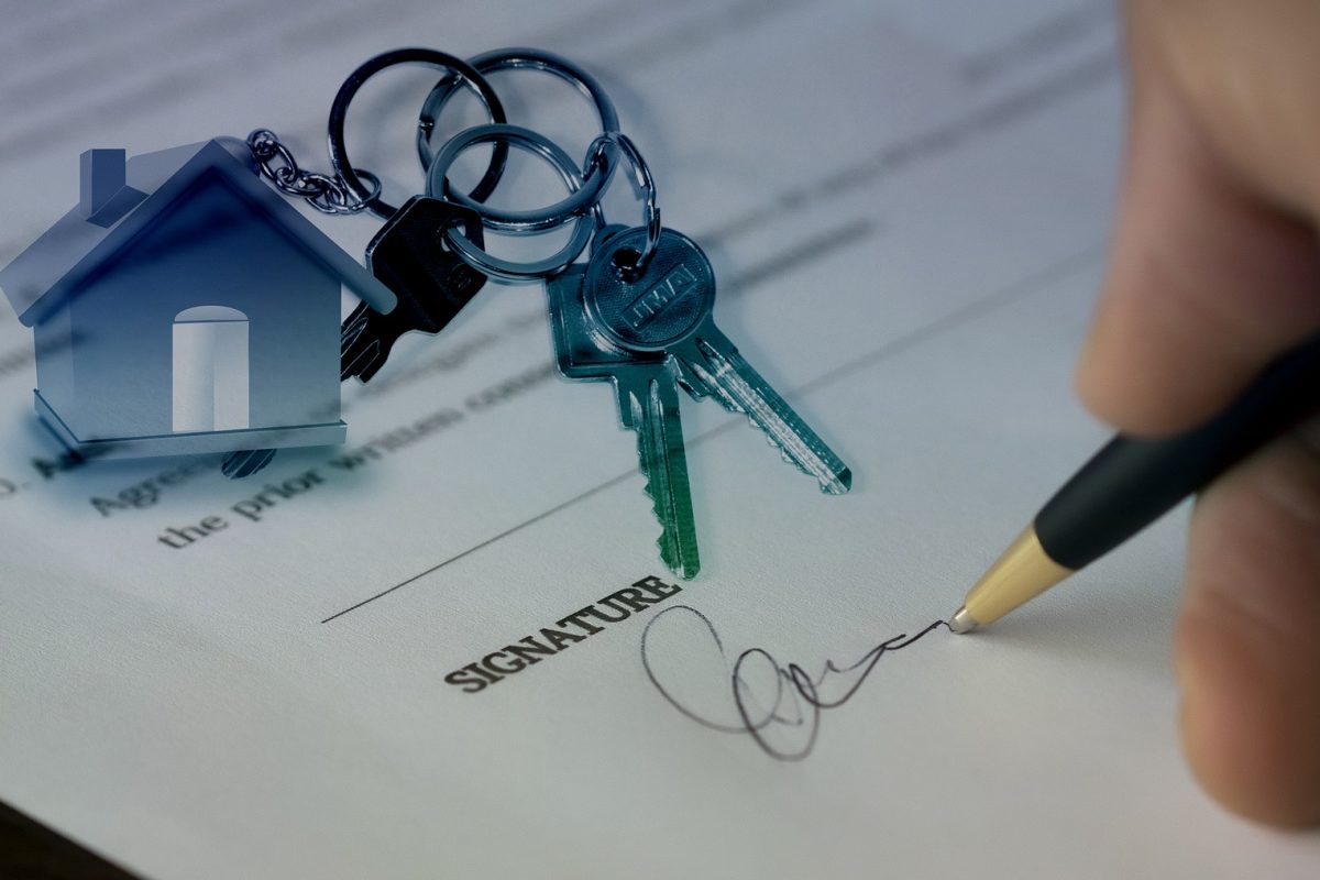 Hand writing signature on paper with keys on a house keychain
