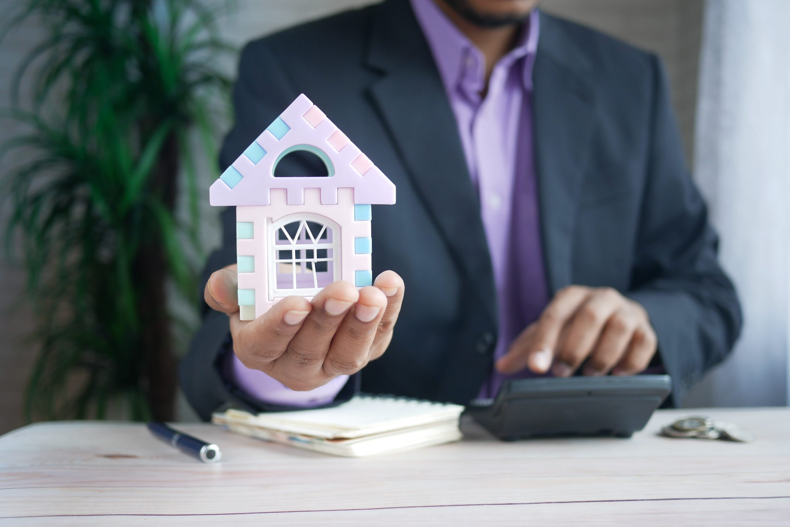 Closeup of Man in a Suit at a Desk Holding a Tiny Toy House